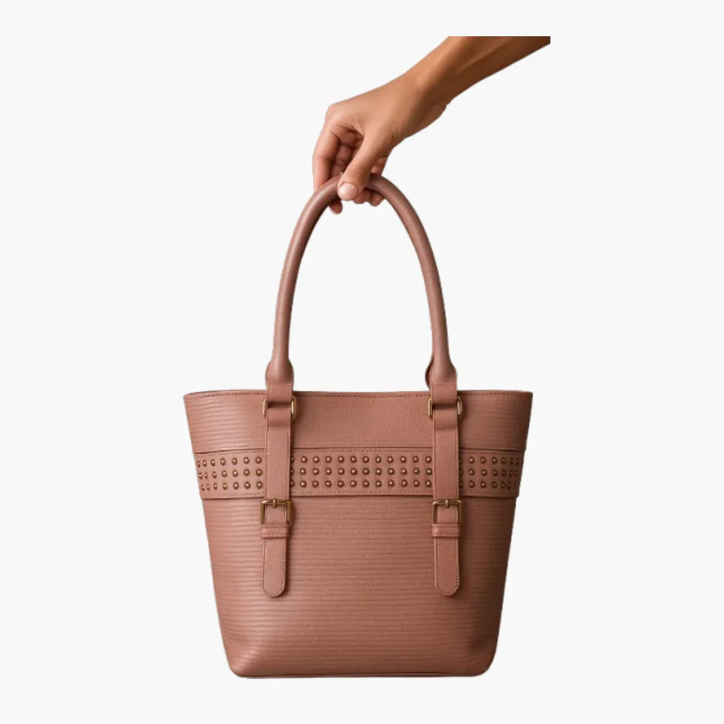 Hand holding a brown premium handbag with gold studs from Bagvalleypk on white background