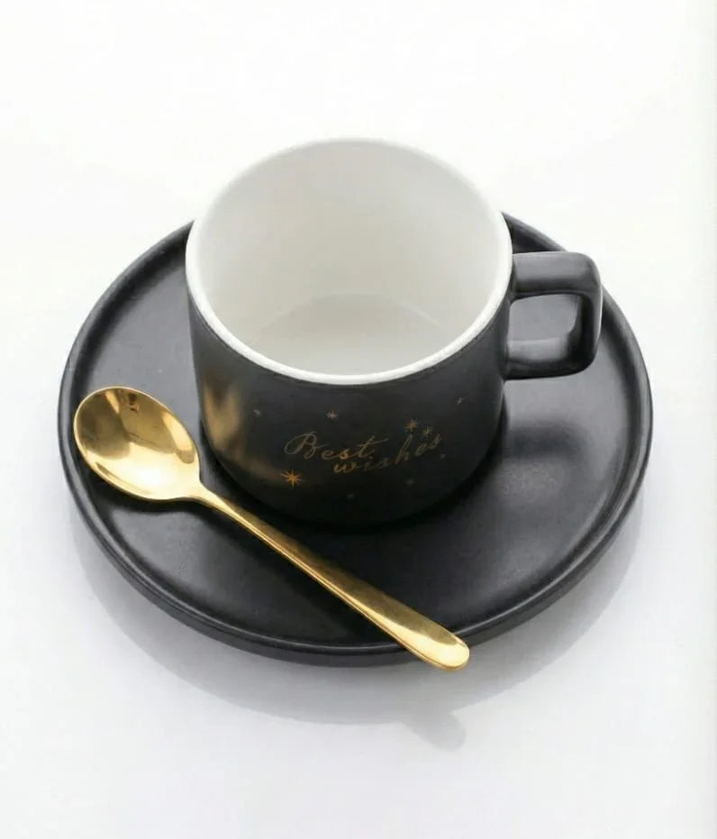 Black ceramic mug with 'Best wishes' text, matching plate, and gold spoon on white background
