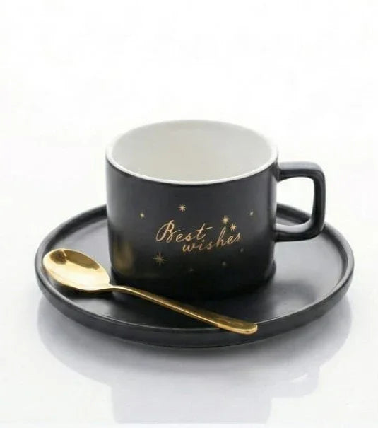 Black ceramic cup with 'Best wishes' gold text, matching saucer, and gold spoon on white background